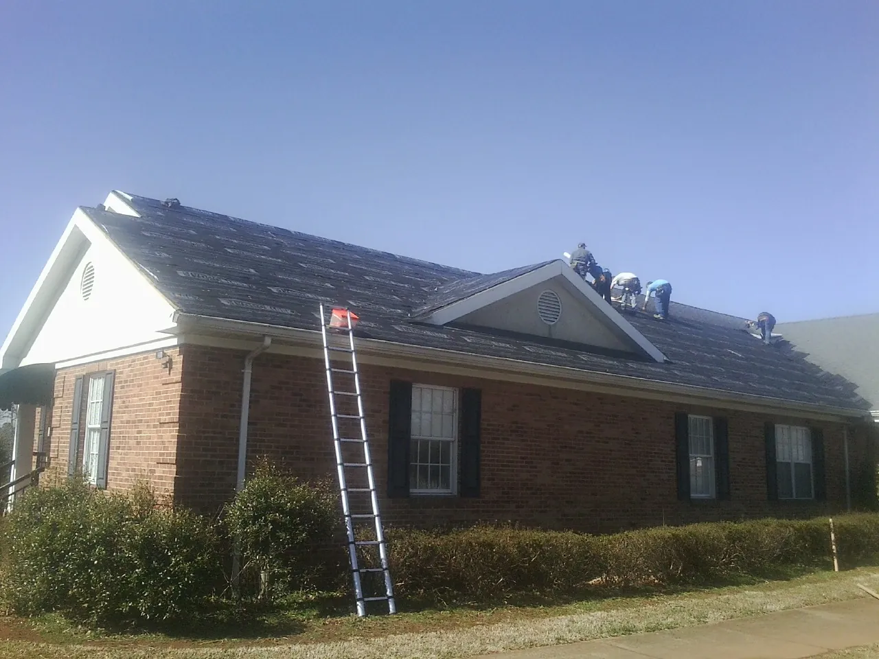 Crew tearing shingles off a brick ranch roof with a ladder set — Emergency Roof Repair work by our crew in Polo