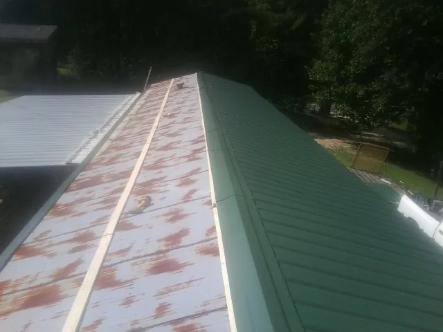 Old rusted panels beside newly installed green metal roofing — Wind Damage Roof Repair by Roofing Brothers in Polo