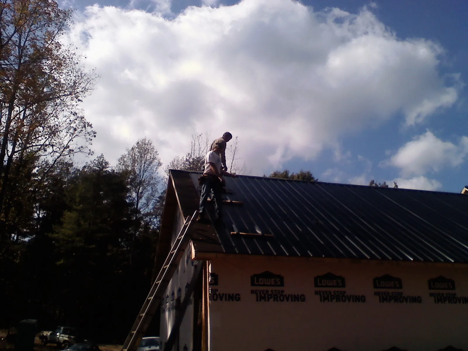 Roofer fastening dark metal panels high against a cloudy sky, from a Roof Inspection job in Polo
