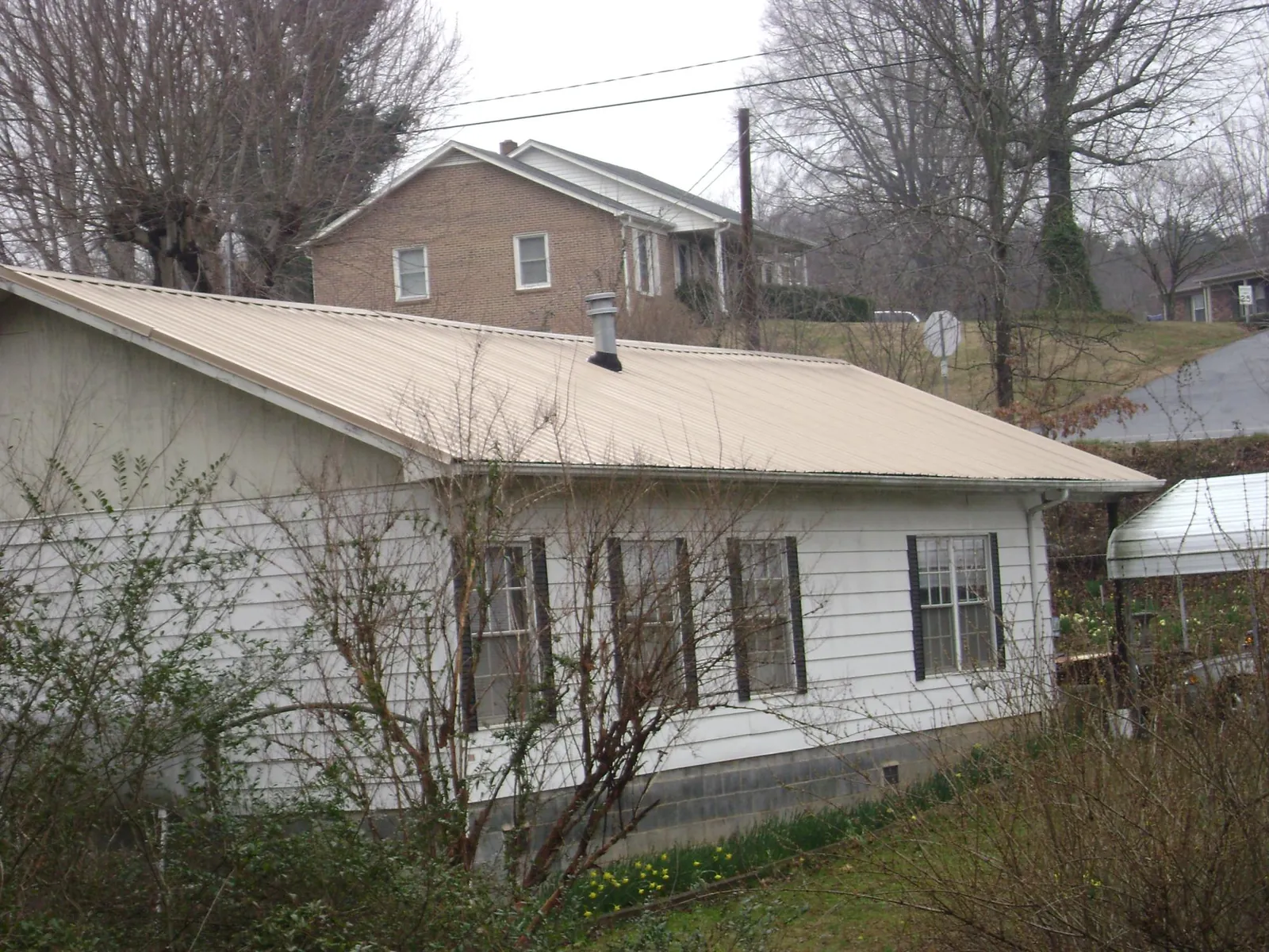 Tan metal roof on a white sided house set into a hillside — Commercial Roofing by Roofing Brothers in Polo